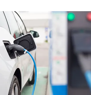 Electric car plugged into Level 2 EV charging station with green light indicator.