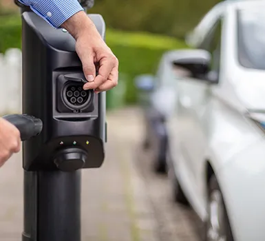 Close-up of hand pressing button on an electric vehicle charging station.