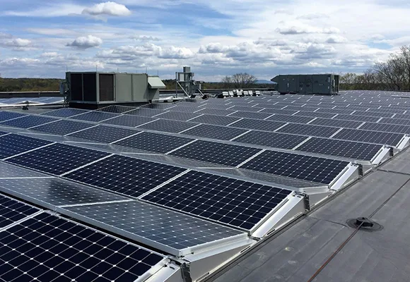 Large array of commercial solar panels installed on a flat rooftop under a partly cloudy sky.