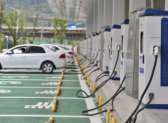 White electric car parked and charging at multiple EV charging stations in a public parking lot.