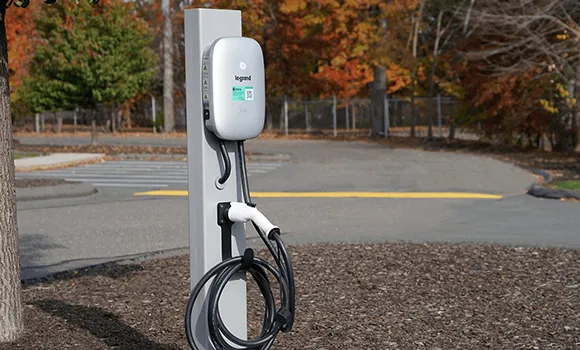 Level 2 electric vehicle charger mounted on a pole in an outdoor parking lot with autumn trees.