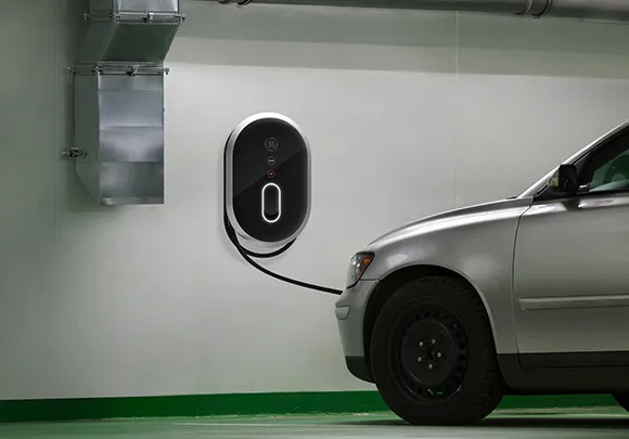 Public electric vehicle charging stations with white and green signage situated in a parking lot with trees in the background.