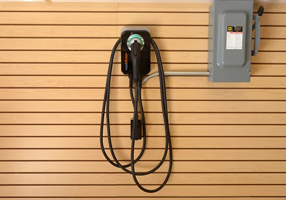 Electric vehicle home charging station mounted on wooden wall with charging cable.