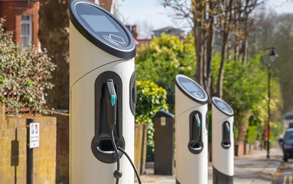 Outdoor level 2 electric vehicle charging stations installed on a sidewalk with greenery in the background.