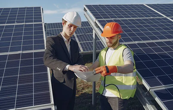 Two professionals in safety gear shaking hands in front of solar panels at a commercial installation site.