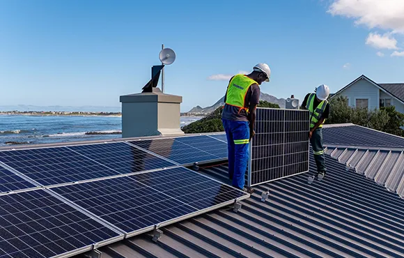 Two workers wearing safety gear installing photovoltaic solar panels on a residential roof, demonstrating the solar panel financing and installation process.