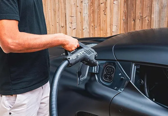 A person plugging a charging cable into an electric vehicle, with a close-up of the charging port and cable.