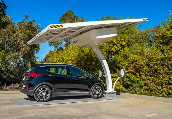 A close-up of an electric vehicle charging cable being plugged into a car, with a charging station in the background.